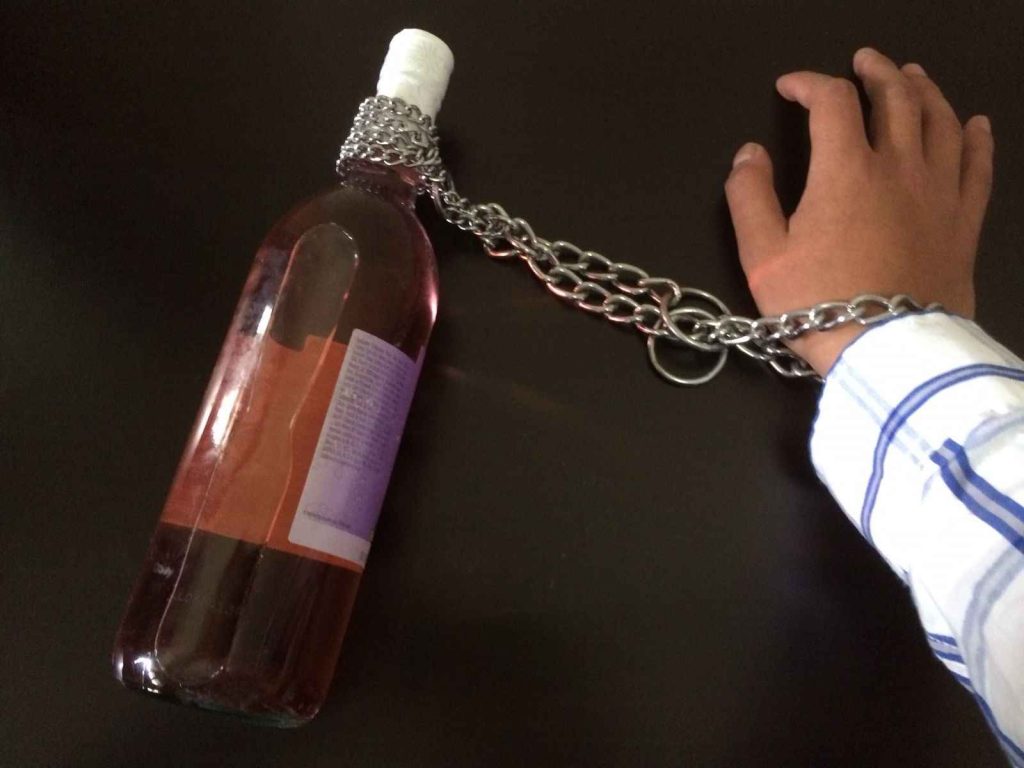 A person's hand is chained to a bottle of wine.