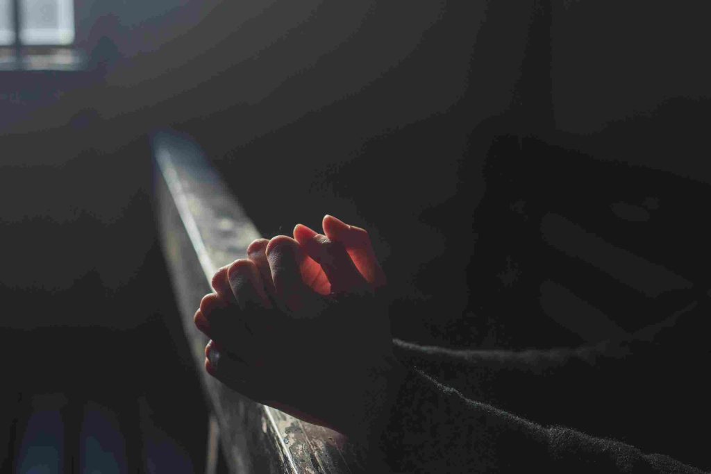A person's hands are clasped together in prayer.